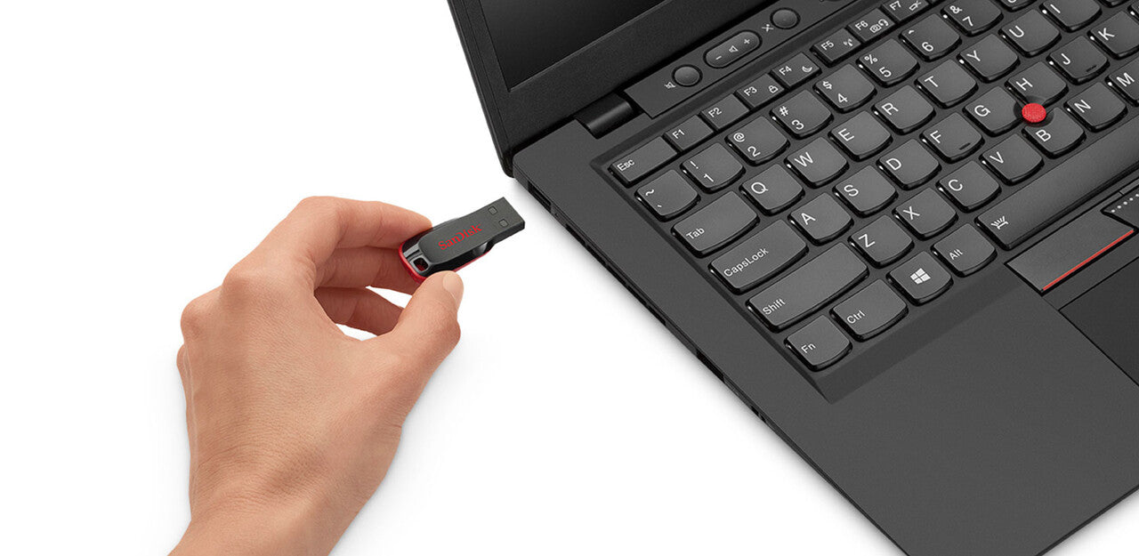 Memoria SanDisk Cruzer Blade negra y roja sostenida junto al puerto USB de una laptop